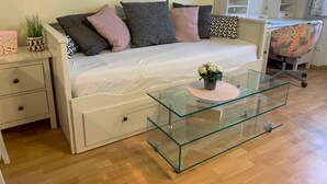A modern living room with a white sofa, glass coffee table, and a white desk with a chair. - Studio mit Garten - Casa Lauda in Bad Vöslau (Bad Vöslau)