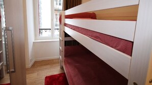 Una cama litera con ropa de cama roja en una habitación con ventana y alfombra roja.
