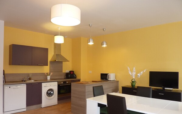 A modern kitchen with a dishwasher, oven, and microwave. There is a dining area with a table and chairs.