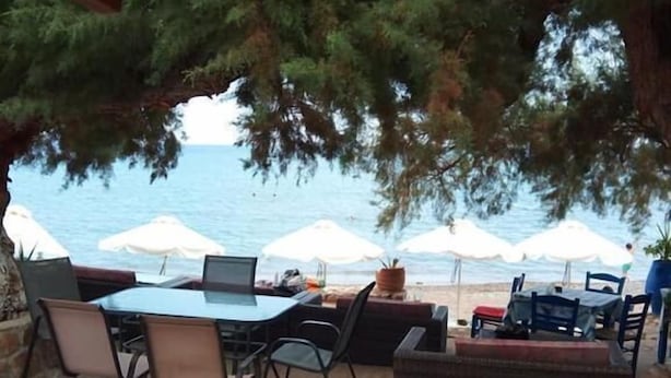 An outdoor seating area with tables and chairs, overlooking a beach with umbrellas. - Beach Front Apartments (Sitia)