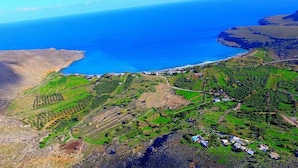 An aerial view of a coastal area with terraced fields, a small settlement, and a clear view of the ocean. - Beach Front Apartments (Sitia)