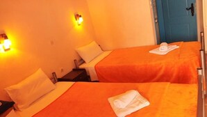 A hotel room with two beds, each with an orange bedspread and a white pillow. There are two wall-mounted lights on either side of the beds. - Beach Front Apartments (Sitia)