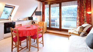 Une pièce chaleureuse comprenant une table à manger, des chaises, un canapé et un balcon avec vue sur les arbres.