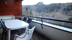 Un balcon avec une table et des chaises blanches, donnant sur un paysage montagneux.