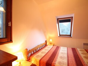 Un dormitorio con cama, mesita de noche, lámpara, ventana y puerta.
