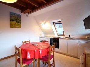 Una cocina con mesa, sillas, ventana y televisor.