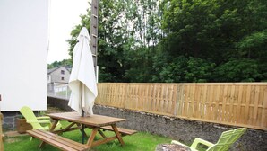 A picnic table with two chairs, a wooden fence, and a tree stump in a grassy area.