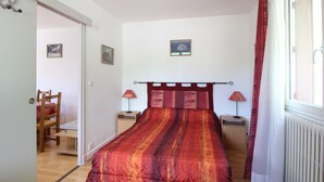 A bedroom with a bed, two bedside tables, a chair, and a window with curtains.