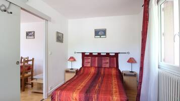 Een slaapkamer met een bed, twee nachtkastjes, een stoel en een raam met gordijnen.