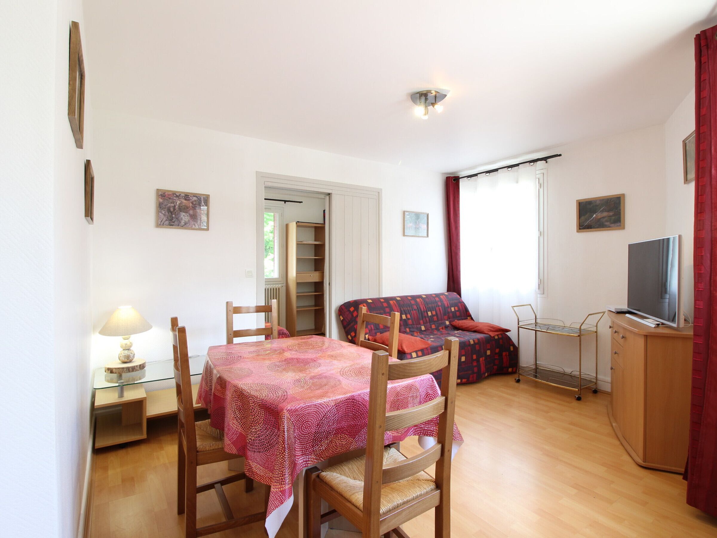 A compact living space with a dining table, chairs, a sofa, a TV, and a small kitchenette.
