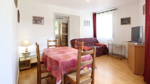 A compact living space with a dining table, chairs, a sofa, a TV, and a small kitchenette.