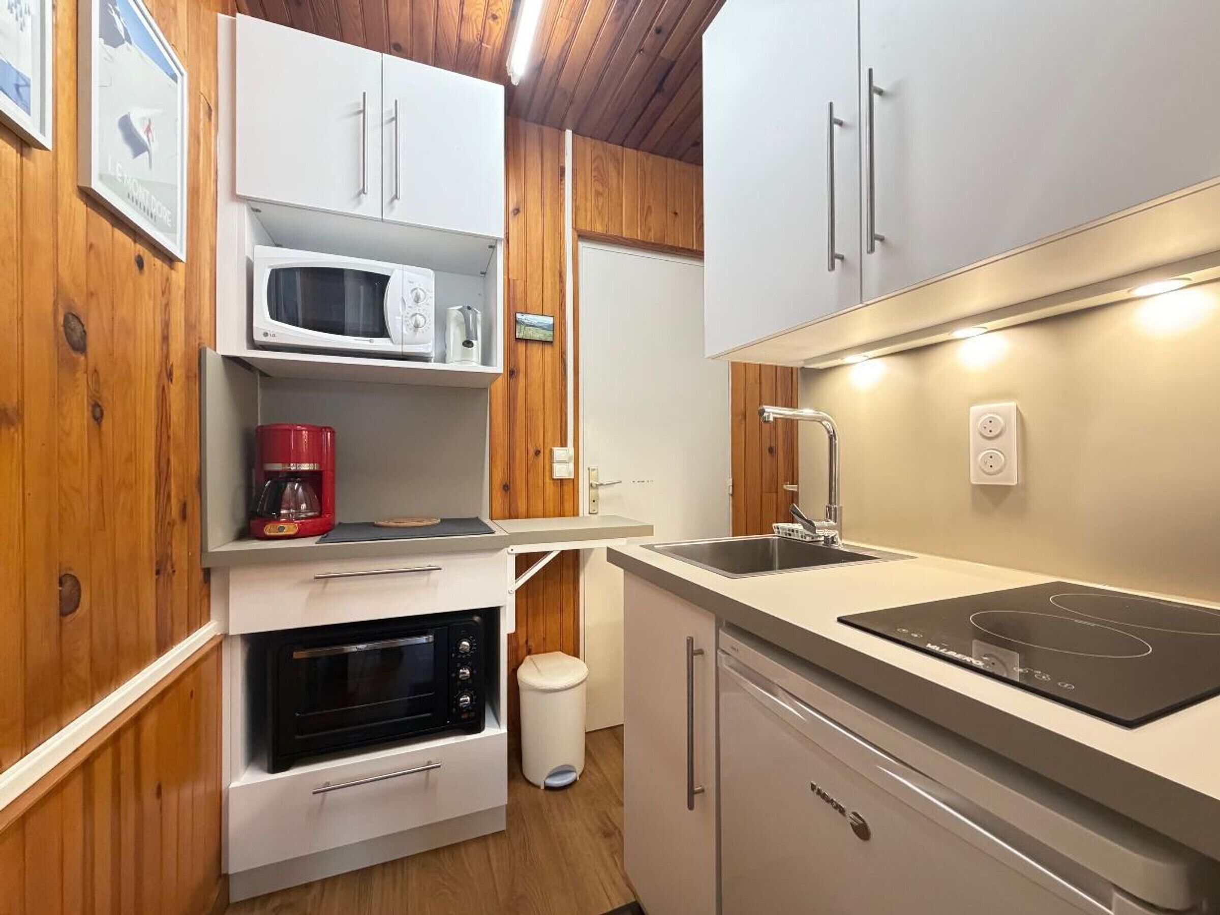 A compact kitchen with white cabinets, a microwave, a coffee maker, a sink, and a stove.