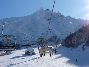 A ski lift with chairs moving up a snowy slope, a mountain in the background, and a clear sky. - 2* Studio in City Center with Balcony & WiFi (Mont-Dore)