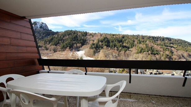 A balcony with a white table and chairs, overlooking a mountainous landscape.