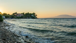 A coastal scene with a rocky shoreline, calm sea, and a building with multiple balconies overlooking the water. - Baywatch Apartments (Zakynthos)