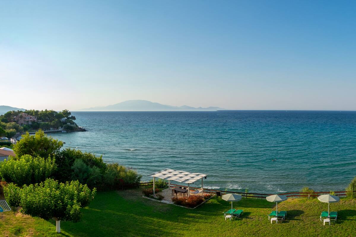 A coastal view with a grassy area, lounge chairs, and umbrellas overlooking the sea.