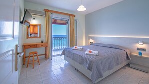 A bedroom with a bed, a desk, a chair, a nightstand, and a view of the sea through a balcony door. - Baywatch Apartments (Zakynthos)