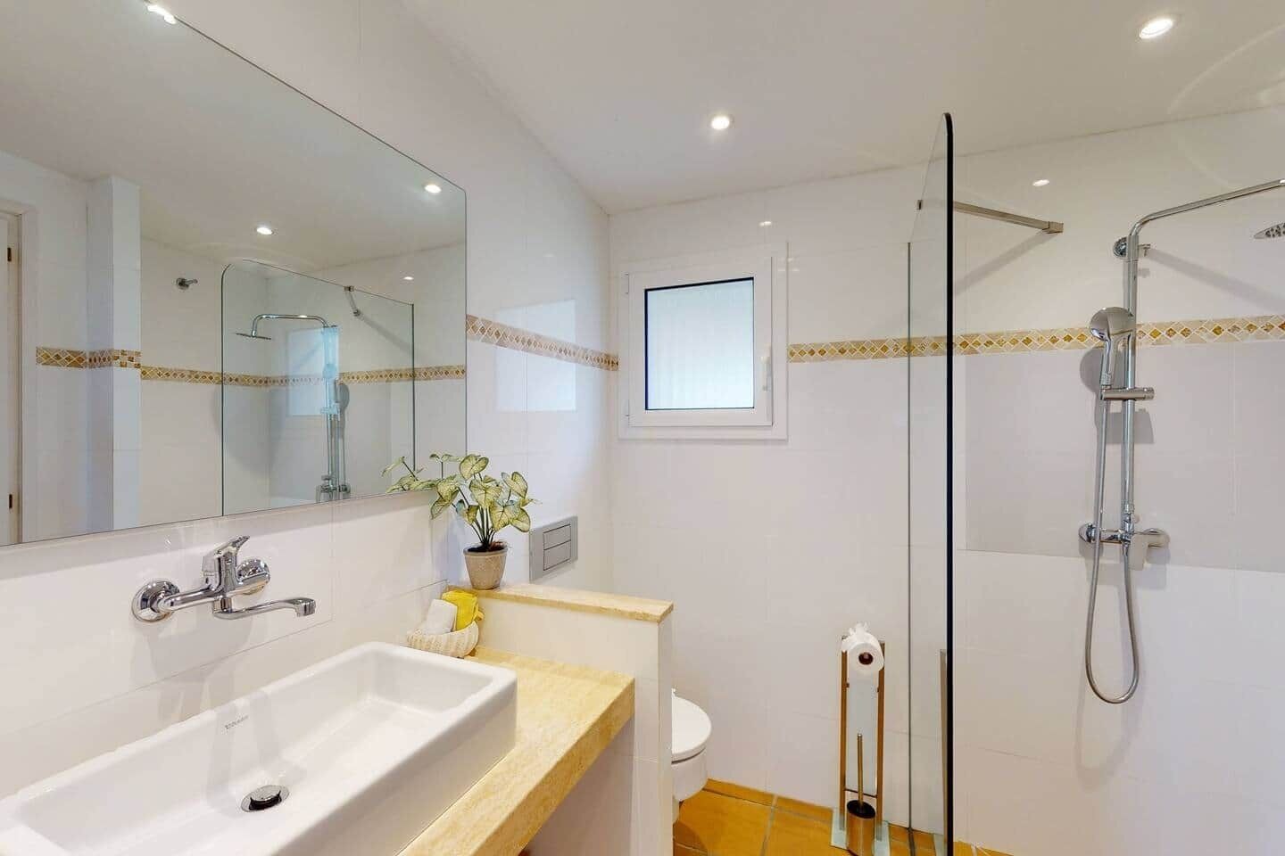 A bathroom with a sink, mirror, toilet, shower, and a potted plant.