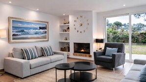 A modern living room with a sofa, armchairs, a fireplace, a bookshelf, and a large painting. - Leo Street 96, Tossa de Mar-Lesal Villas Rentals Mar Azul (Santa maria de llorell, tossa de mar, gi)