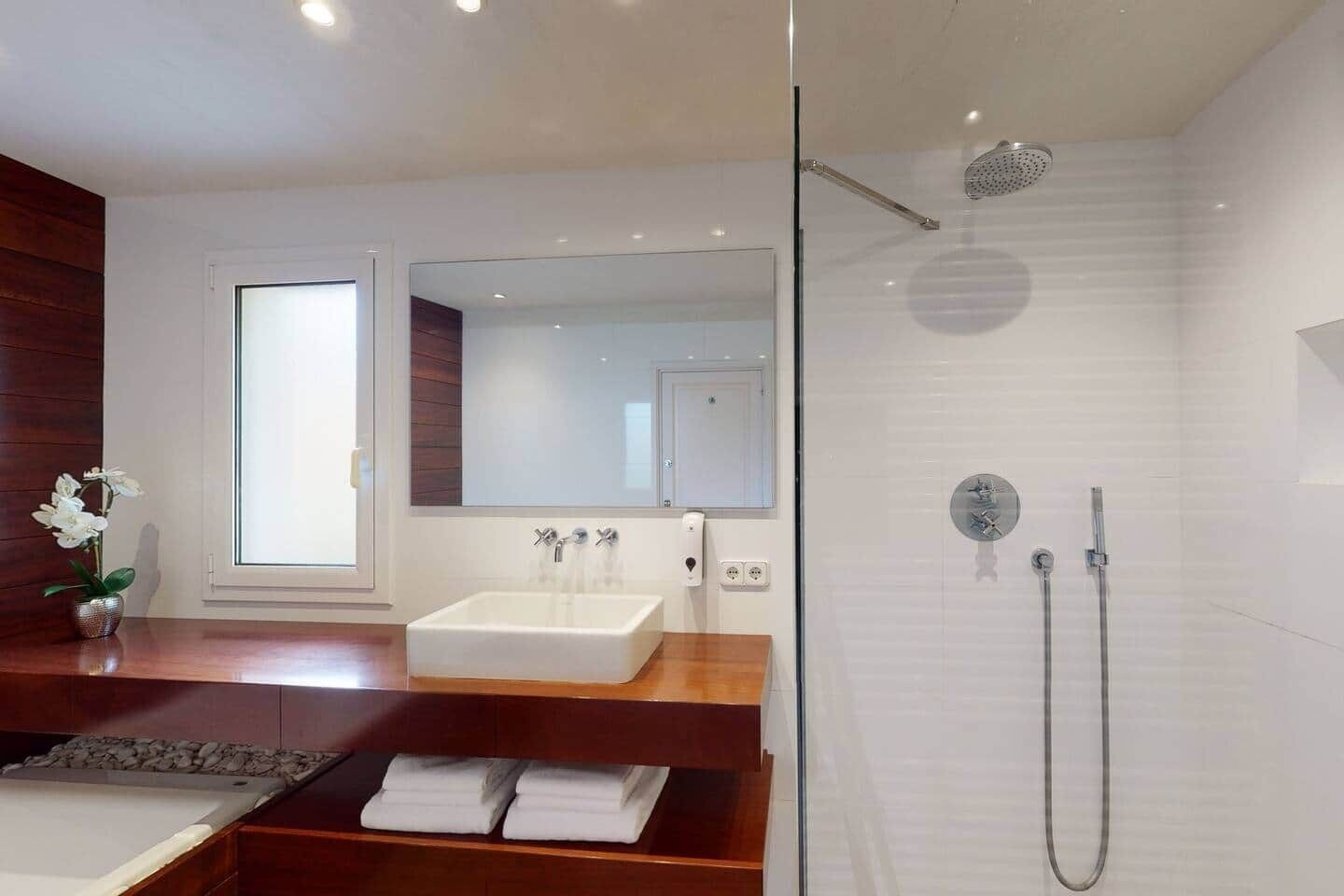 Ein modernes Badezimmer mit einer ein Glasfach umschlossenen Dusche, einem großen Spiegel und einem Holzlagerplatz mit einem weißen Waschbecken.