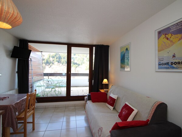 A living room with a sofa, a dining table, and a view of a balcony.