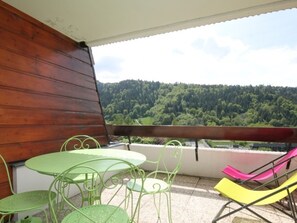 A balcony with a wooden wall, a table with chairs, and a view of a forested hill.
