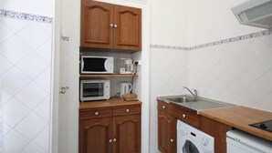 Cocina compacta con armarios de madera, microondas, cafetera, lavadora y lavaplatos.
