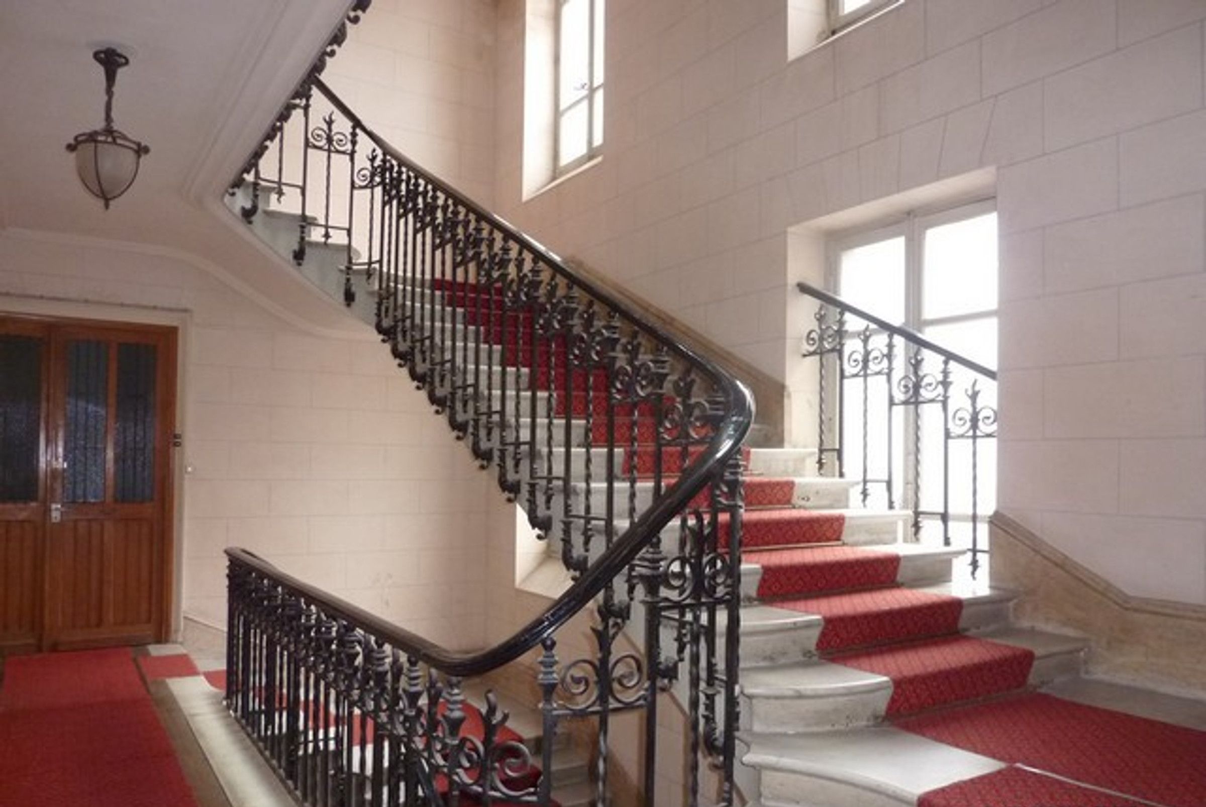 Eine prachtvolle Treppe mit aufwendigen schwarzen Geländern und roten Teppichstufen, die zu einem Podest mit einer Holztür und einem Fenster führt.