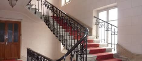 Eine prachtvolle Treppe mit aufwendigen schwarzen Geländern und roten Teppichstufen, die zu einem Podest mit einer Holztür und einem Fenster führt.