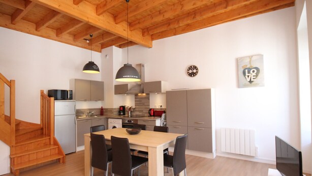 Una cocina moderna con vigas de madera, un comedor con mesa y sillas, microondas y cafetera.