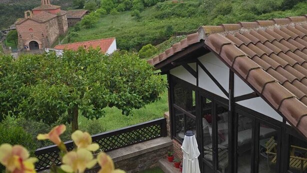 Una terraza con vistas a un valle exuberante, un edificio de piedra y una estructura con paredes de cristal.