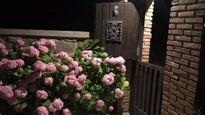 Un muro de ladrillo con una reja metálica decorativa, suelo de baldosas estampadas y macizos de hortensias rosas.