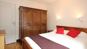 Een slaapkamer met een houten kledingkast, een bed met rode kussens en een nachtkastje.