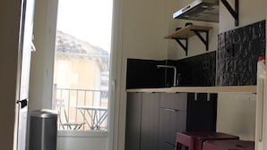 Une petite cuisine étroite avec un seul tabouret de bar, une poubelle et une fenêtre donnant sur un balcon.