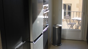 Une cuisine équipée d’un réfrigérateur en acier inoxydable, d’une poubelle et d’une porte donnant sur un balcon avec une table et des chaises.
