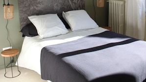 Une chambre à coucher avec un lit, une lampe fixée au mur et une grande tapisserie.