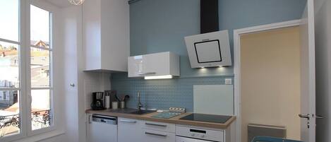 A modern kitchen with white cabinets, a wooden countertop, and a blue backsplash. There is a window providing natural light, and a door leading to another room.