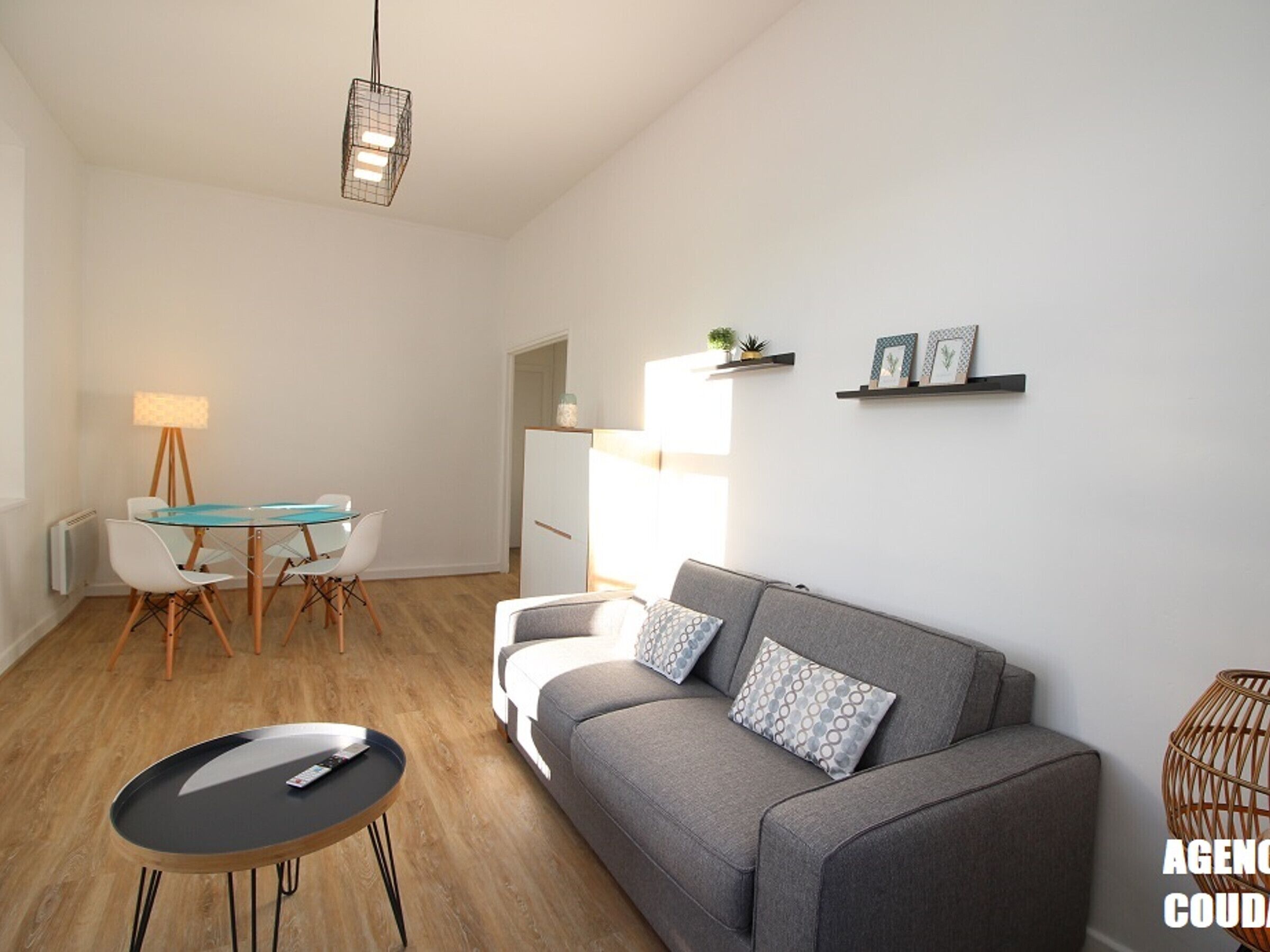 A modern living room with a grey sofa, a glass dining table, and a black coffee table.