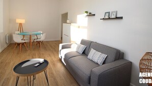 Ein modernes Wohnzimmer mit einem grauen Sofa, einem Glastisch und einem schwarzen Couchtisch.