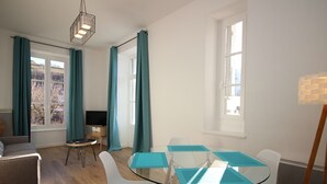 Ein modernes Wohnzimmer mit einem Glastisch, weißen Stühlen, einer Couch und einem Fernseher auf einem Schrank.