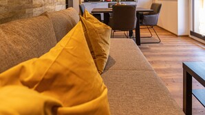 A modern living room with a sofa, yellow cushions, a dining area with chairs, and a kitchen in the background. - Tevini Boutique Suites by we rent (Zell am See)