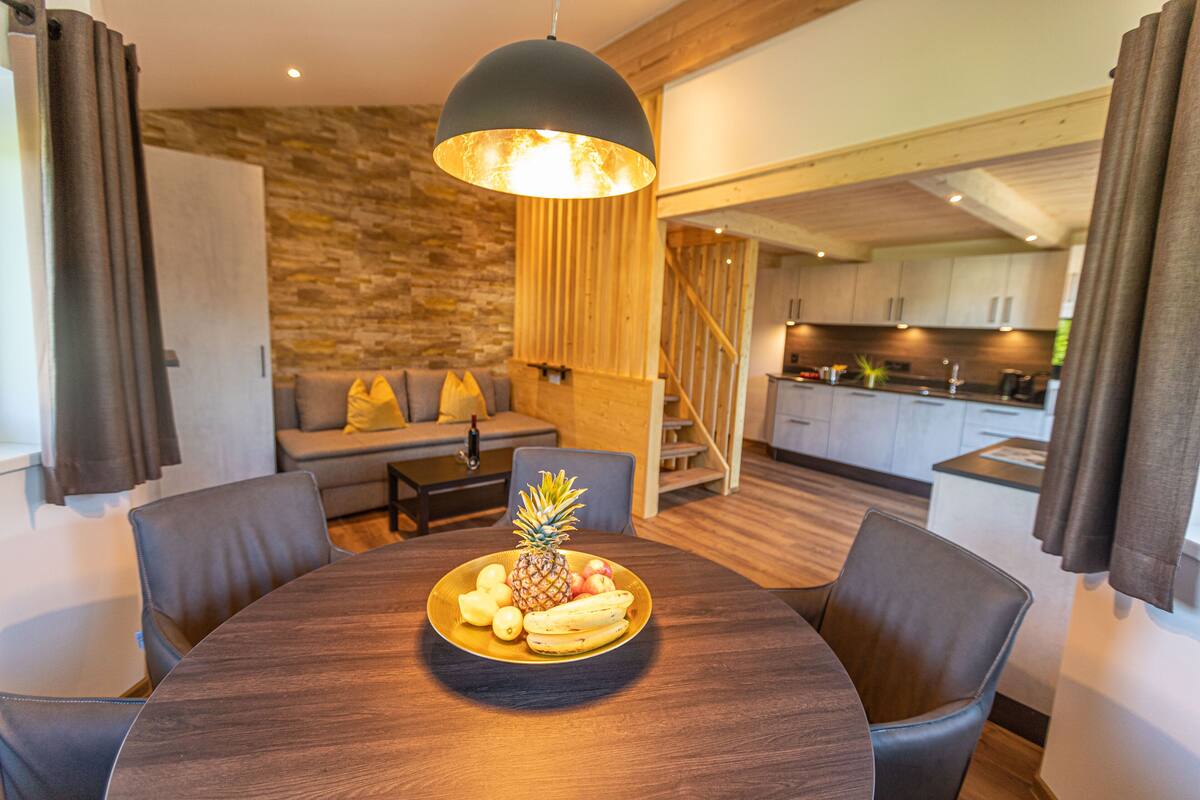 Un coin repas avec une table ronde, un panier de fruits et un luminaire suspendu moderne.