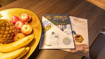 A table with a fruit bowl containing bananas, apples, and a pineapple, and two brochures titled "Zell am See Gold Edition" and "Pinzgau".