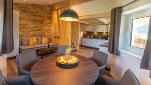 A modern dining area with a round table, dark chairs, and a fruit bowl centerpiece. - Tevini Boutique Suites by we rent (Zell am See)