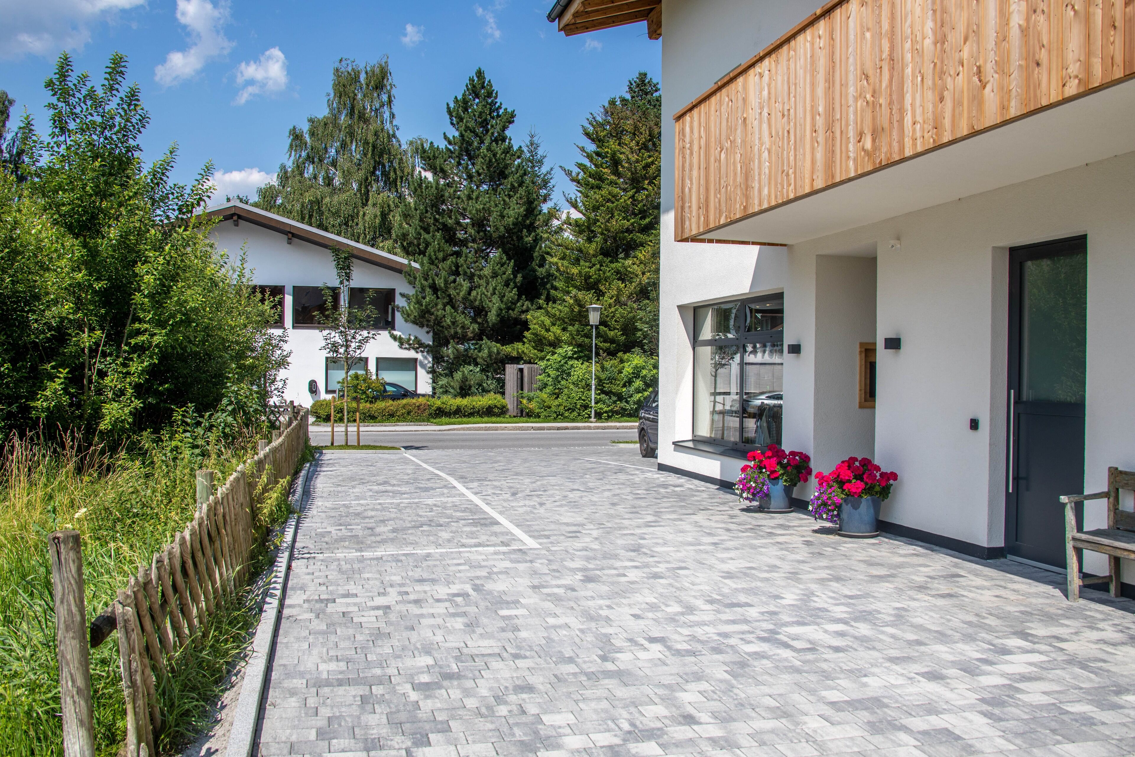 A modern building with a paved walkway, wooden fence, and potted plants.