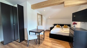 A modern hotel room with a bed, a desk, a chair, a wardrobe, and a flat-screen TV. - Tevini Boutique Suites by we rent (Zell am See)