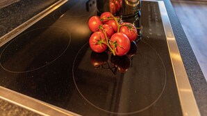 A kitchen with a stovetop, a pot, and tomatoes on the counter. - Tevini Boutique Suites by we rent (Zell am See)