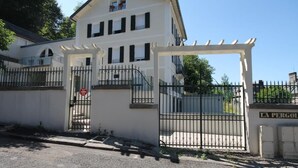 Un bâtiment à deux étages, doté d’une entrée fermée par un portail, d’une enseigne indiquant « LA PERGOLA » et surplombant un ciel dégagé.