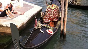 Una góndola amarrada en un muelle de un canal, con edificios al fondo.