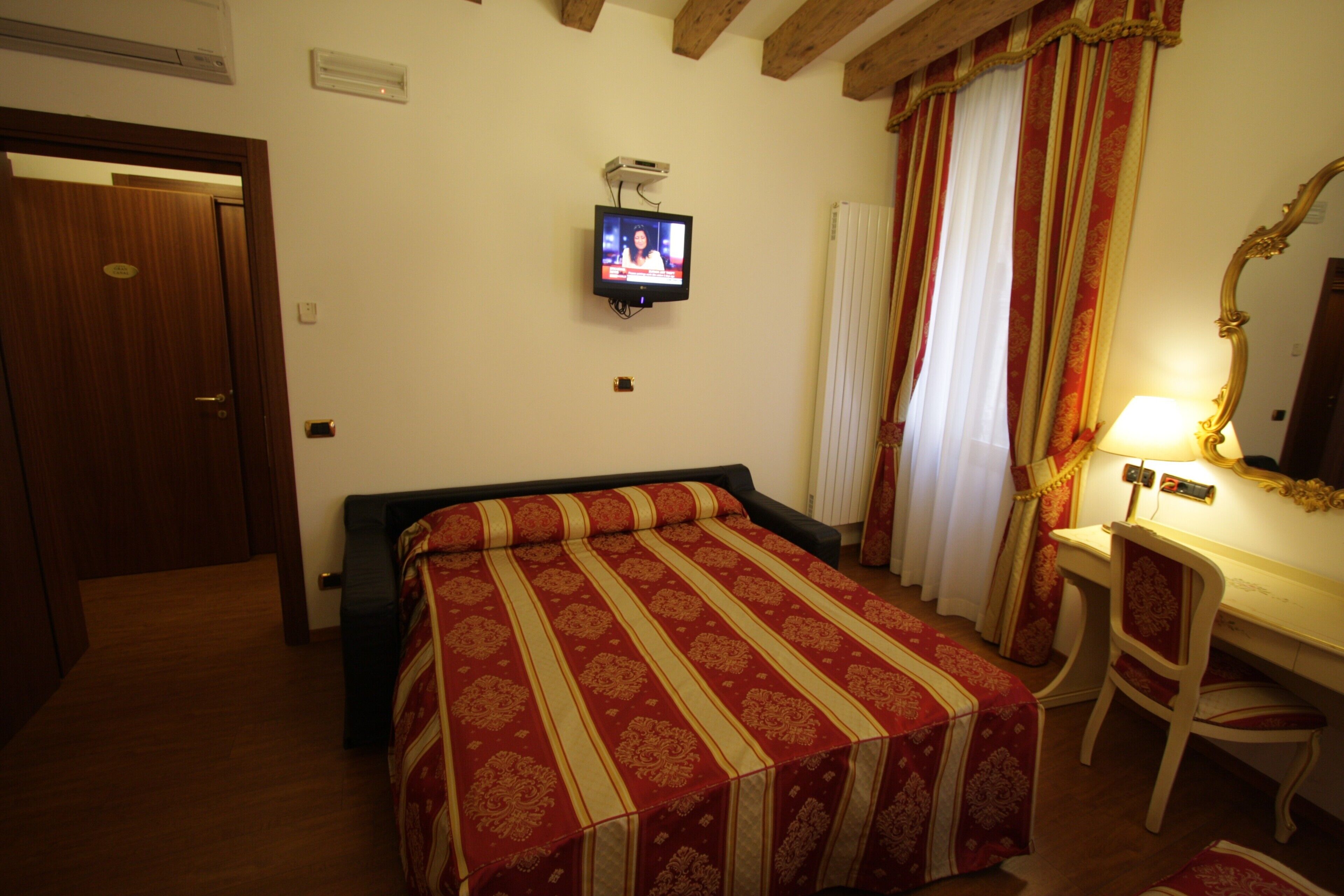 Une chambre d’hôtel équipée d’un lit, d’un bureau, d’une chaise, d’une télévision et d’un miroir.